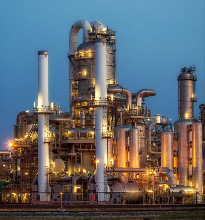 Refinaria iluminada ao anoitecer, com torres e tubulações